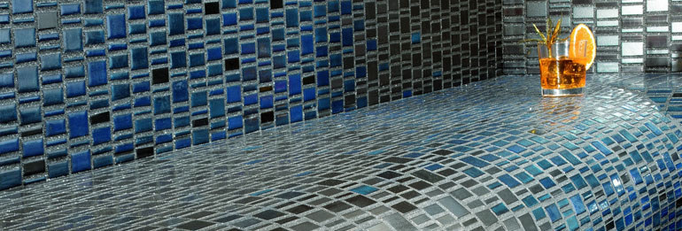 Eine Sitzbank im blauen Mosaik mit einem Cocktailglas verziert.