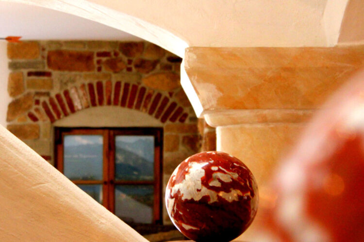 Dekorative Kugel auf einem Sockel vor einem Fenster mit gemauertem Rundbogen in warmem Licht.