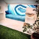 Liege mit Hinterleuchteter Glasplatte mit blausteinoptik. Sehr schön dekoriert mit Pflanzen und Palmen. rechts auf einem Sockel steht ein silberner Waschtisch.