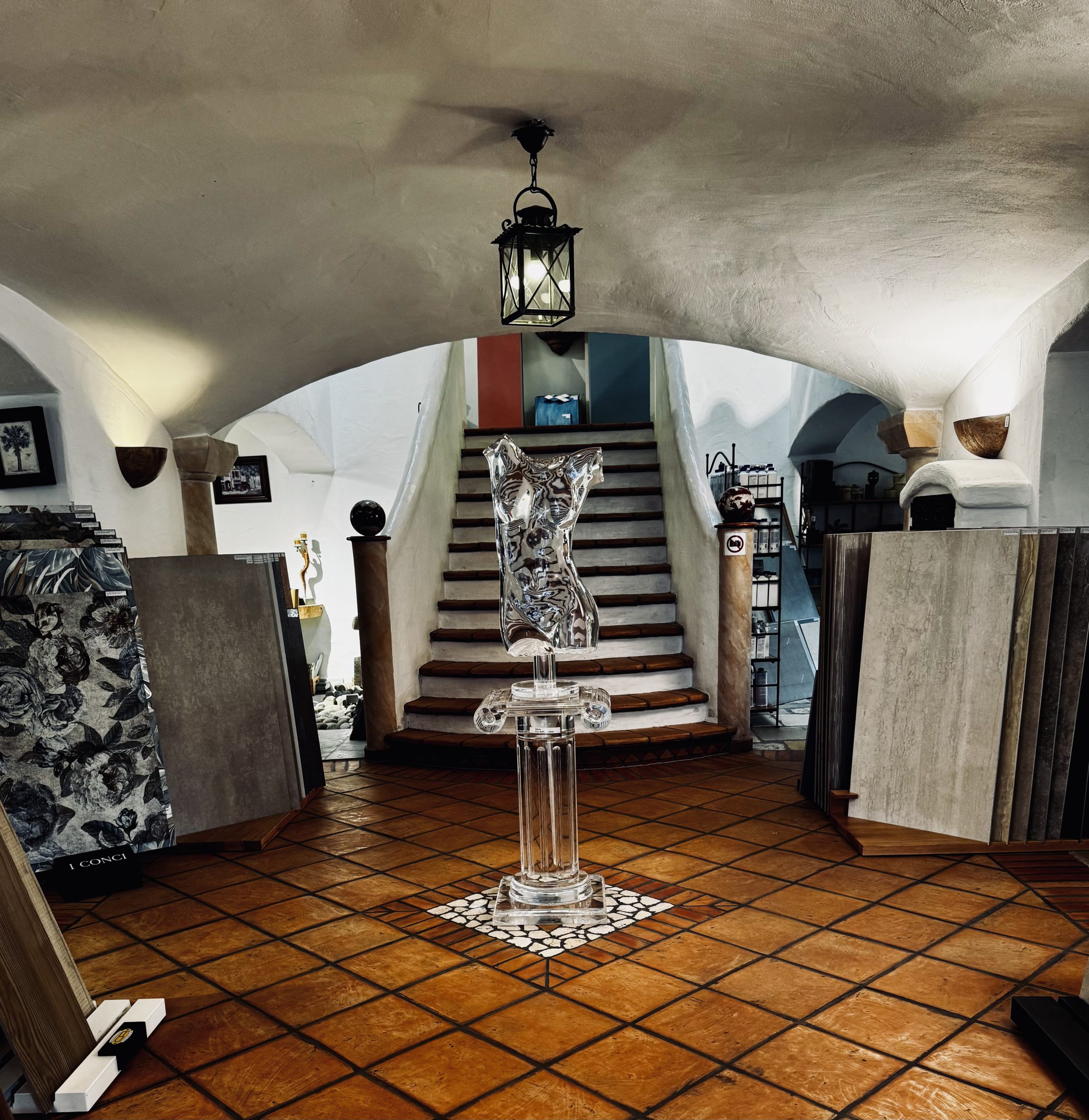 Eingangsbereich der Ausstellung im Erdgeschoss mit Cotto Boden . Zu sehen sind einige Fliesenmuster und eine Acrylskulptur in Form eines Oberkörpers.