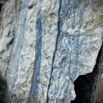Ein großer, grob behauener Block aus hellem Naturstein mit markanten, senkrecht verlaufenden blauen Streifen. die Oberfläche ist rau und uneben, mit sichtbaren Bruchkanten und natürlichen Adern. Der Stein zeugt eine Mischung aus hellgrauen und bläulichen Farbtönen. Es handelt sich um einen Quarzit