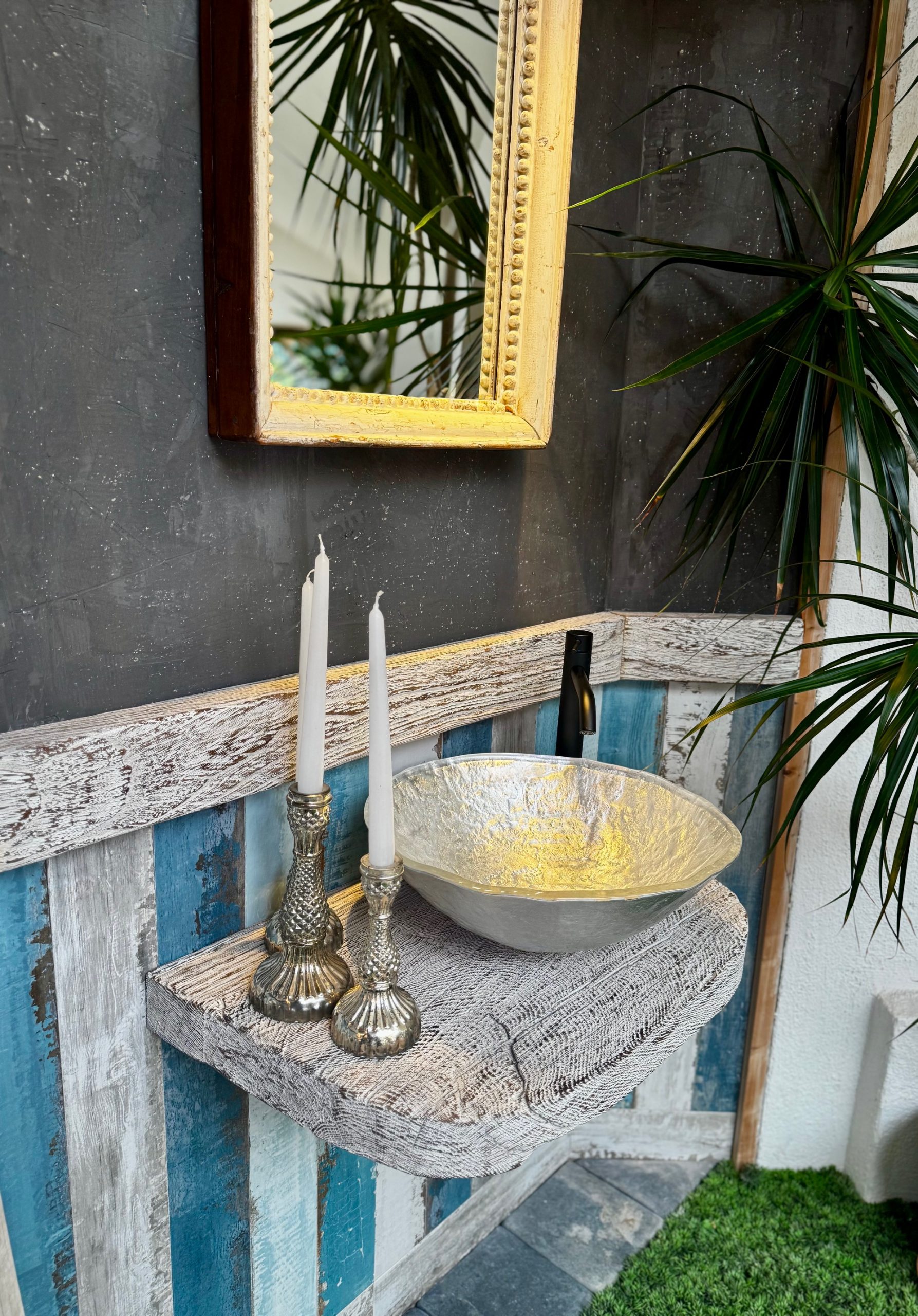 Badezimmermuster mit Silbernen Glaswaschtisch auf einem an der Wandmontierten Holzbrett. Die Rückwand ist gefliest in Holzoptik in verschiedenen blautönen.